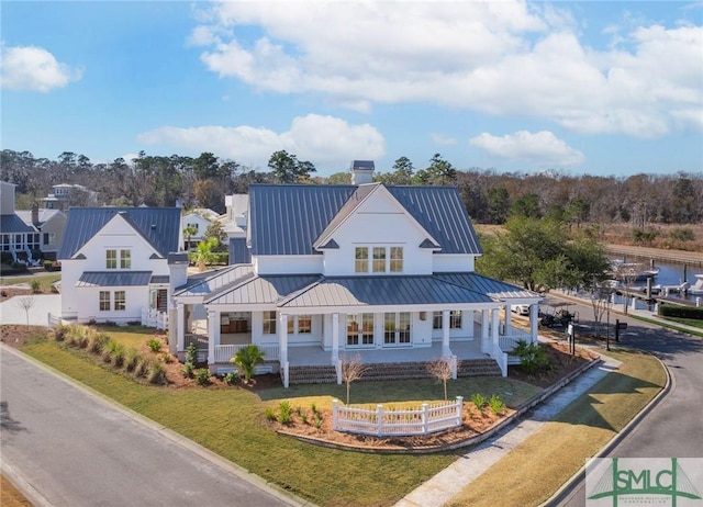 exterior space featuring a chimney, metal roof, a standing seam roof, a porch, and a front yard