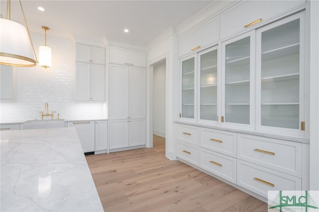 kitchen featuring light wood-style flooring, a sink, white cabinetry, hanging light fixtures, and light stone countertops