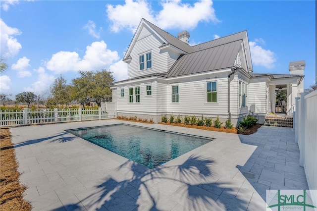 rear view of house with metal roof, a patio, fence, a fenced in pool, and a standing seam roof