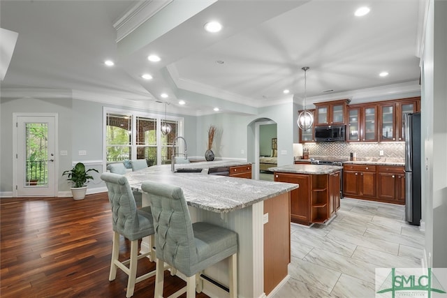 kitchen with light stone countertops, a kitchen island, stainless steel appliances, decorative light fixtures, and light hardwood / wood-style flooring