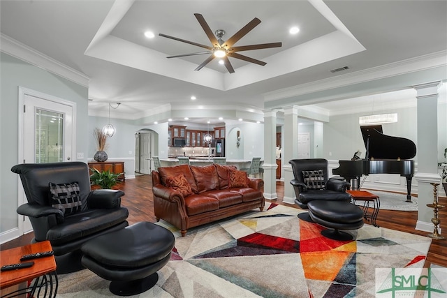 living room featuring decorative columns, a raised ceiling, ornamental molding, and ceiling fan with notable chandelier