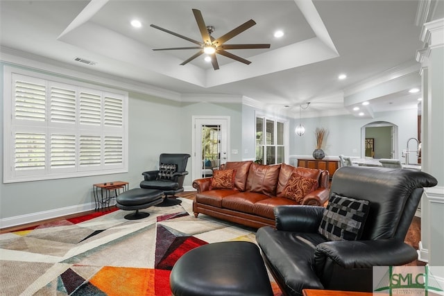 living room with crown molding, a tray ceiling, a healthy amount of sunlight, and ceiling fan