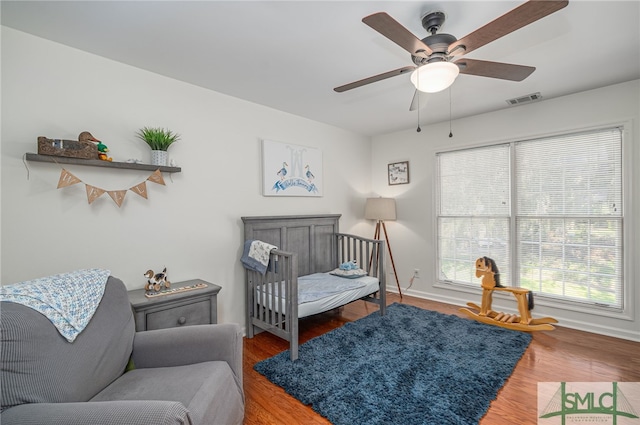 bedroom with ceiling fan, hardwood / wood-style floors, and a nursery area