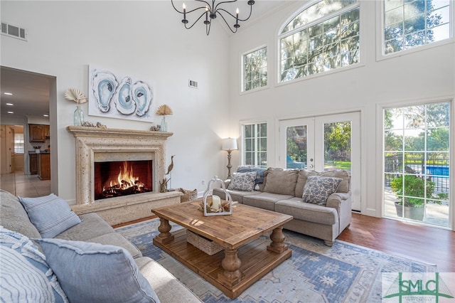 living room featuring a high ceiling, french doors, hardwood / wood-style floors, a notable chandelier, and a fireplace