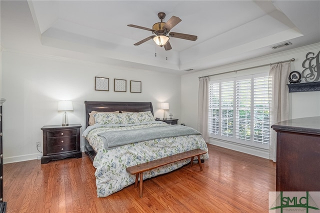 bedroom featuring ornamental molding, hardwood / wood-style floors, ceiling fan, and a raised ceiling