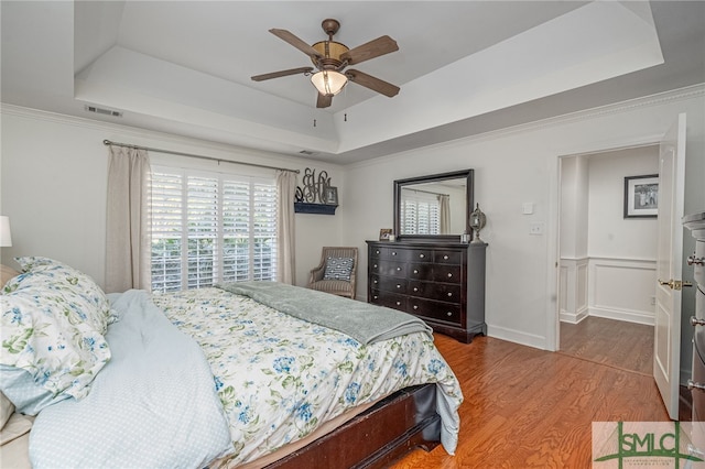 bedroom with crown molding, wood-type flooring, a tray ceiling, and ceiling fan