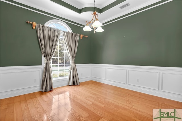 unfurnished room with ornamental molding, a chandelier, hardwood / wood-style flooring, and a raised ceiling