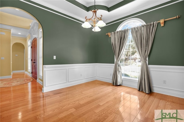 empty room with a notable chandelier, ornamental molding, and light hardwood / wood-style flooring