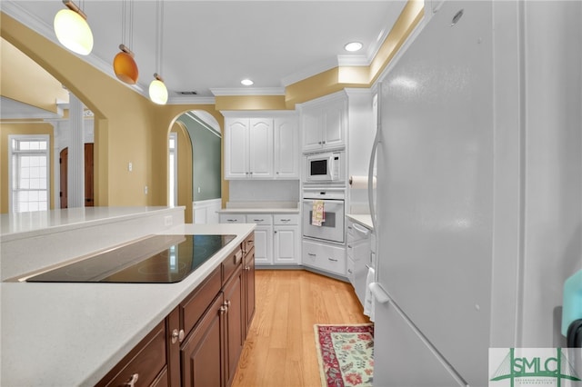 kitchen with white cabinets, hanging light fixtures, light hardwood / wood-style flooring, crown molding, and white appliances