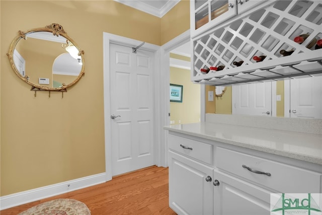 bar with white cabinetry, light hardwood / wood-style floors, ornamental molding, and light stone counters