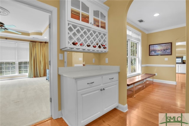 bar featuring ceiling fan, crown molding, light wood-type flooring, and white cabinets