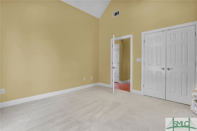 unfurnished bedroom featuring a closet, high vaulted ceiling, and light colored carpet