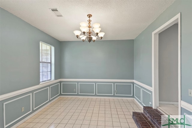 empty room with light tile patterned flooring, a textured ceiling, and an inviting chandelier