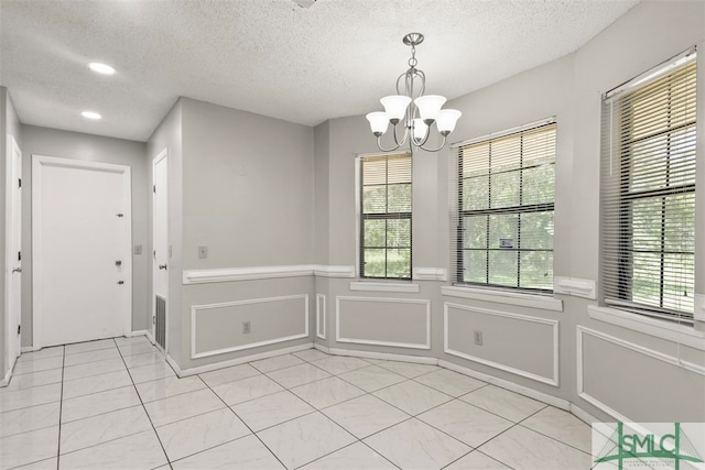 unfurnished dining area featuring a healthy amount of sunlight, an inviting chandelier, and a textured ceiling