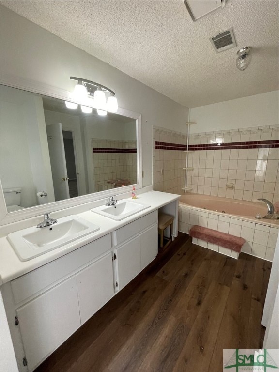 bathroom with a bath, vanity, a textured ceiling, hardwood / wood-style flooring, and toilet