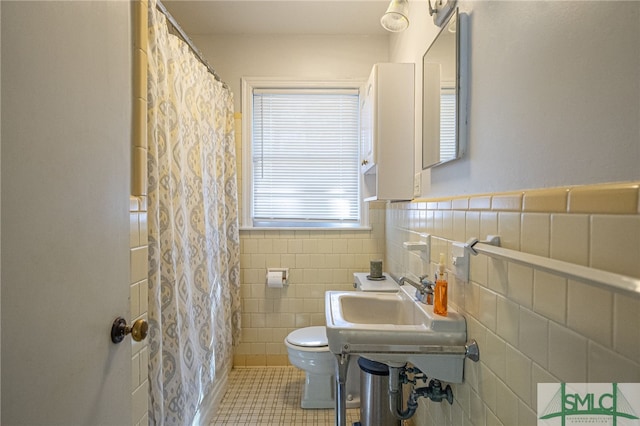 bathroom featuring toilet, tile patterned flooring, sink, curtained shower, and tile walls