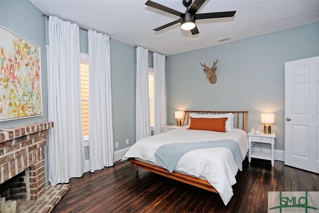 bedroom featuring dark hardwood / wood-style flooring, a brick fireplace, and ceiling fan