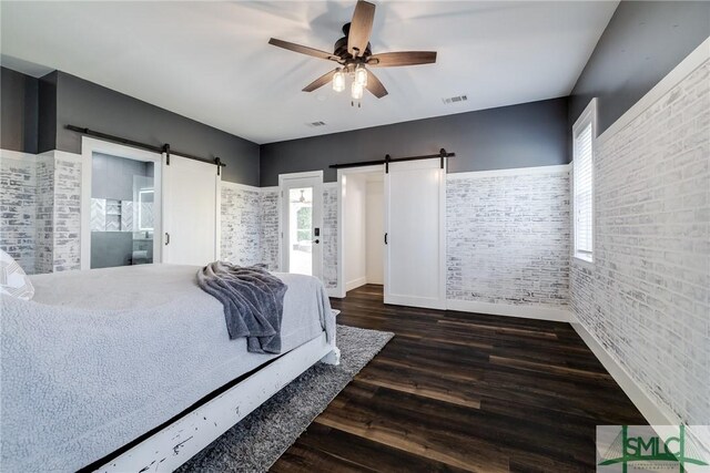 bedroom featuring dark wood-type flooring, a barn door, brick wall, and ceiling fan