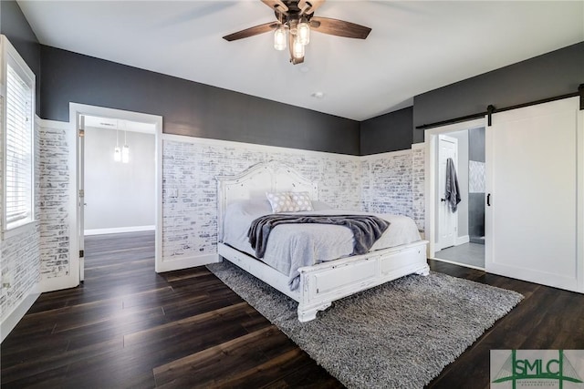 bedroom featuring a barn door, dark hardwood / wood-style floors, ceiling fan, and brick wall