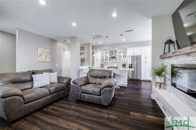 living room with a stone fireplace, a barn door, and dark wood-type flooring