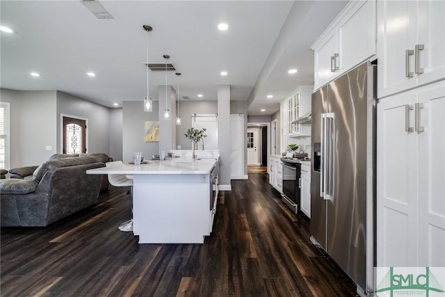 kitchen featuring pendant lighting, white cabinets, an island with sink, appliances with stainless steel finishes, and dark hardwood / wood-style flooring