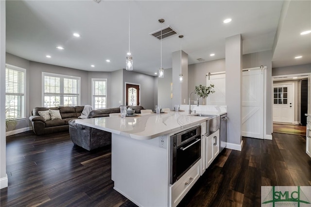 kitchen with dark hardwood / wood-style floors, oven, a barn door, pendant lighting, and white cabinetry