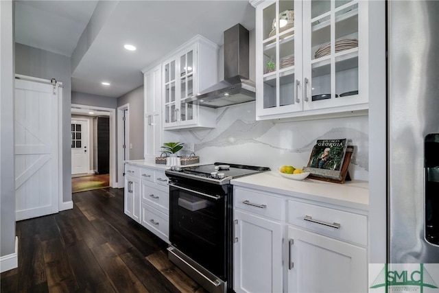 kitchen with dark hardwood / wood-style flooring, electric range oven, wall chimney range hood, a barn door, and white cabinetry