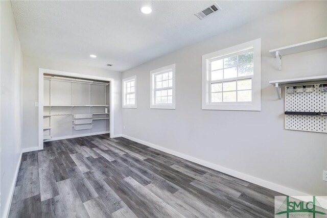 unfurnished bedroom featuring multiple windows, dark hardwood / wood-style floors, and a closet