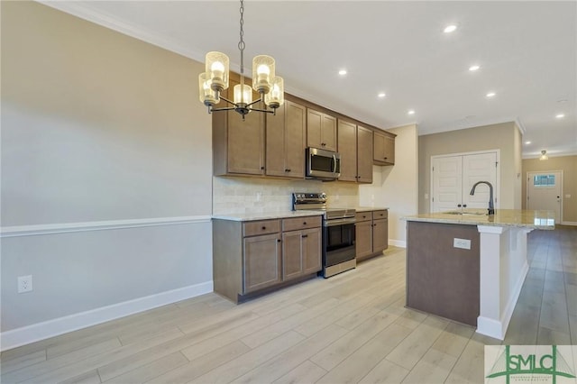 kitchen with appliances with stainless steel finishes, tasteful backsplash, sink, light stone countertops, and a center island with sink