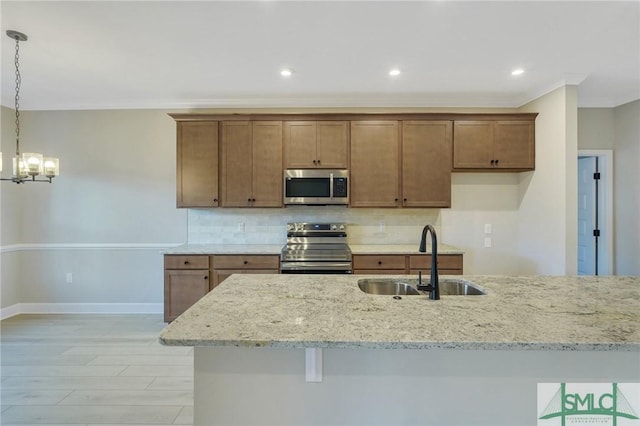 kitchen featuring sink, tasteful backsplash, light stone counters, hanging light fixtures, and appliances with stainless steel finishes