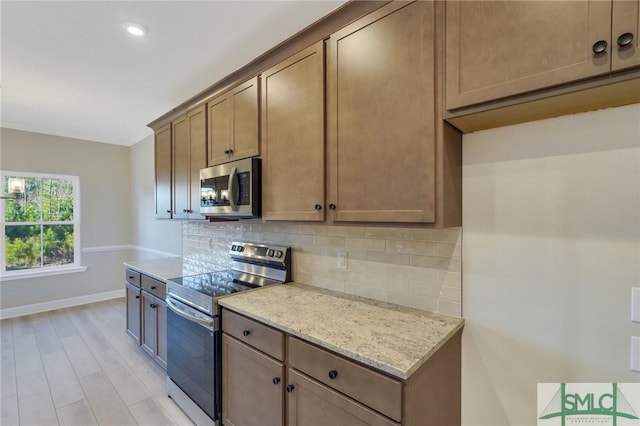 kitchen featuring tasteful backsplash, light stone countertops, stainless steel appliances, and light hardwood / wood-style floors