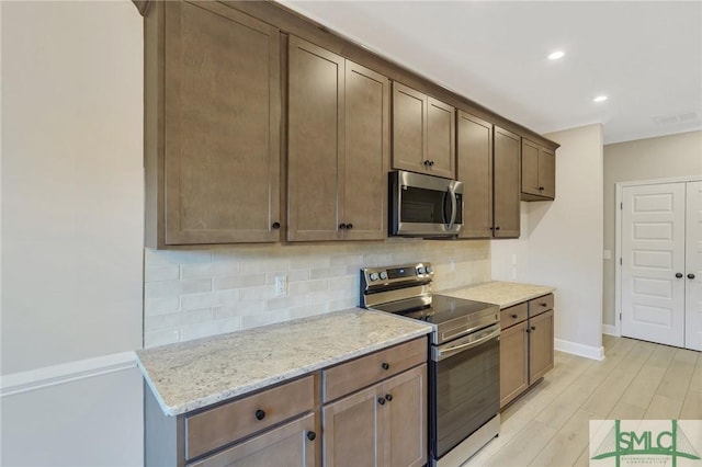 kitchen featuring tasteful backsplash, appliances with stainless steel finishes, light wood-type flooring, and light stone counters