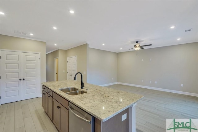 kitchen with dishwasher, light stone countertops, sink, and a center island with sink