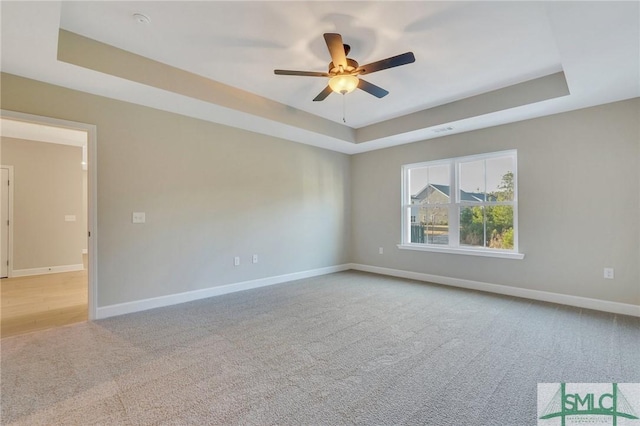 carpeted spare room with ceiling fan and a tray ceiling