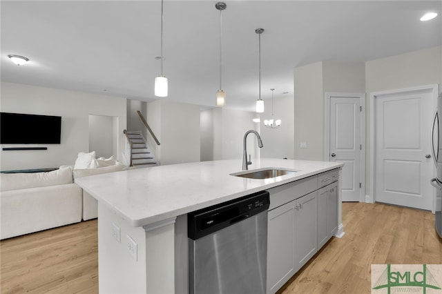 kitchen featuring hanging light fixtures, a center island with sink, sink, stainless steel dishwasher, and light hardwood / wood-style floors