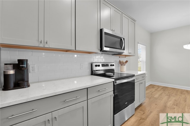 kitchen with appliances with stainless steel finishes, light hardwood / wood-style flooring, tasteful backsplash, and gray cabinetry