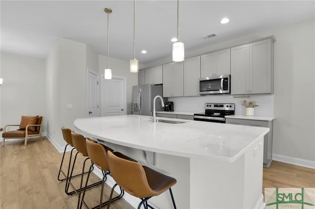 kitchen with stainless steel appliances, light hardwood / wood-style flooring, pendant lighting, and an island with sink