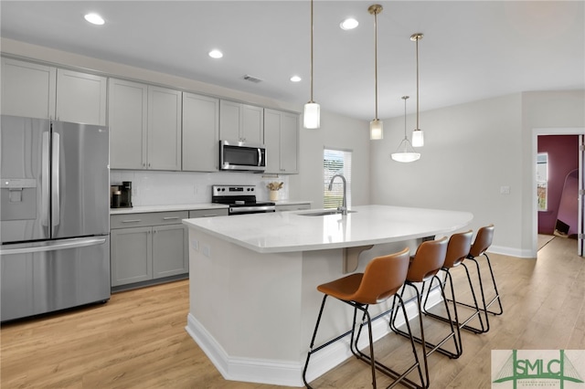 kitchen featuring hanging light fixtures, appliances with stainless steel finishes, a kitchen island with sink, gray cabinetry, and sink