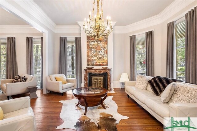 living room with an inviting chandelier, dark wood-type flooring, ornamental molding, and a healthy amount of sunlight