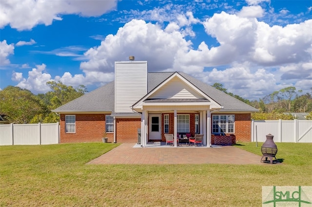 rear view of property featuring a yard, a patio, and an outdoor fire pit