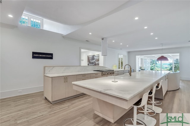 kitchen featuring a large island, sink, a breakfast bar, light wood-type flooring, and stainless steel gas stovetop