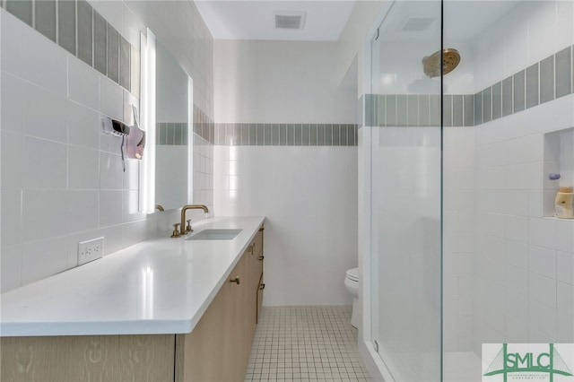 bathroom with tile patterned floors, toilet, vanity, tile walls, and an enclosed shower