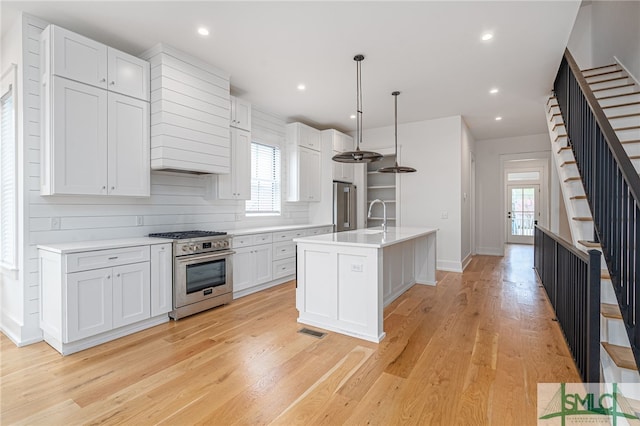 kitchen featuring white cabinetry, appliances with stainless steel finishes, light hardwood / wood-style flooring, and an island with sink