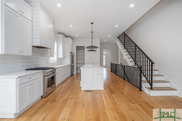 kitchen with white cabinets, a center island with sink, appliances with stainless steel finishes, light wood-type flooring, and decorative light fixtures