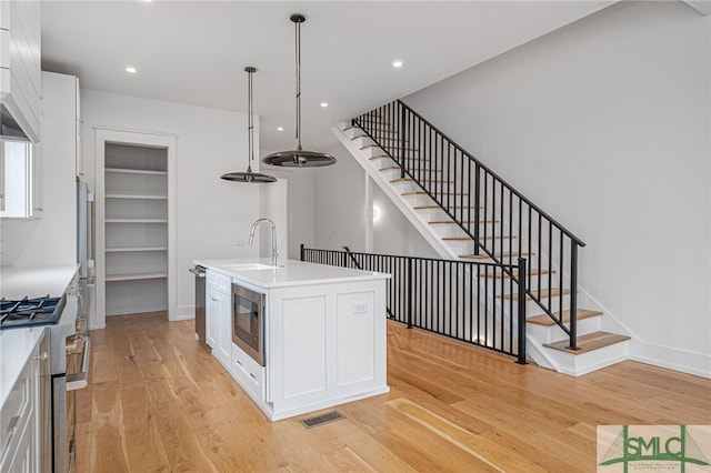 kitchen with white cabinetry, light wood-type flooring, and an island with sink