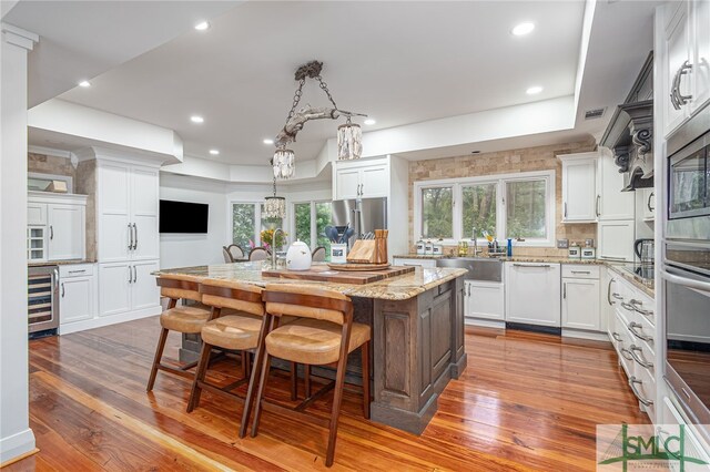 kitchen with hardwood / wood-style floors, a kitchen breakfast bar, stainless steel appliances, wine cooler, and a sink