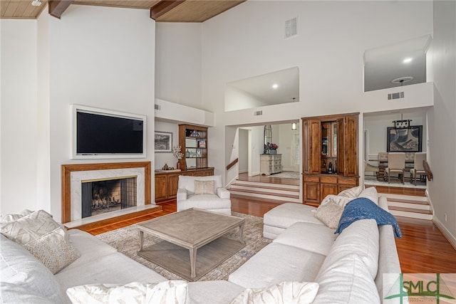 living room featuring beamed ceiling, a premium fireplace, light wood-type flooring, and high vaulted ceiling