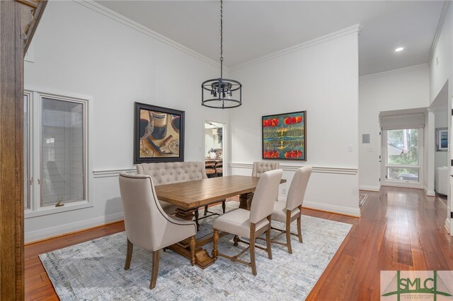 dining space with wood finished floors, a high ceiling, crown molding, and a notable chandelier