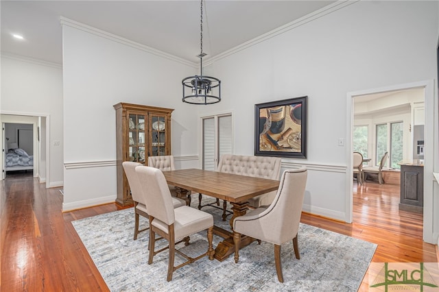 dining space featuring wood-type flooring, a high ceiling, an inviting chandelier, and ornamental molding