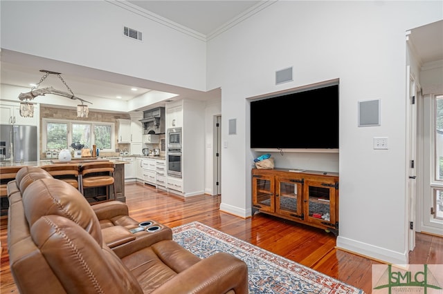 living room featuring ornamental molding, hardwood / wood-style flooring, and a towering ceiling